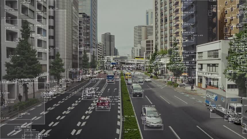 A cityscape with flowing traffic is analyzed by AI software, highlighting vehicles with tracking boxes and data