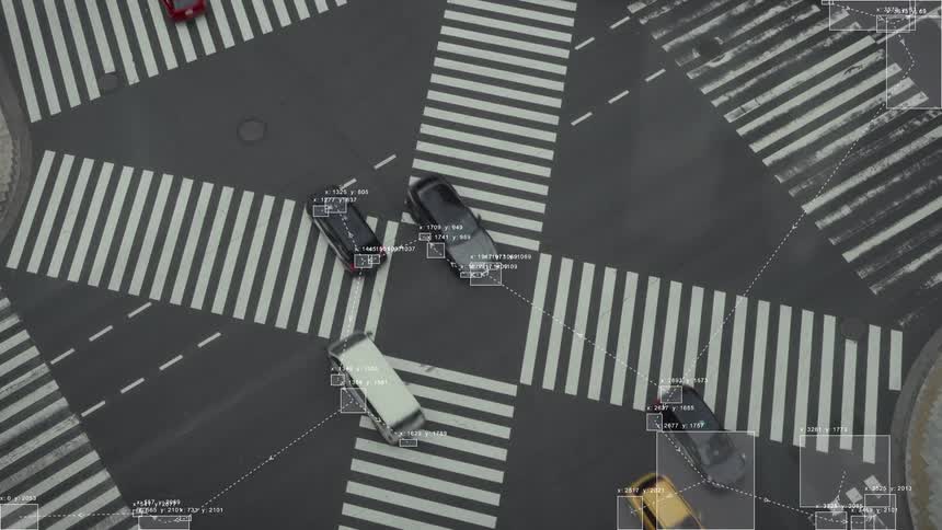 An aerial view shows a sophisticated traffic surveillance system using AI to track cars at a busy city intersection