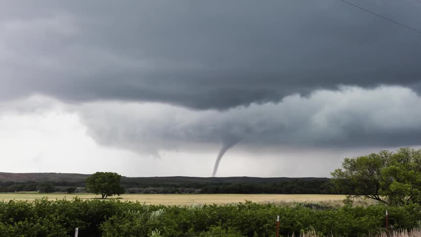 A tornado touches ground while storm clouds circle over a field
