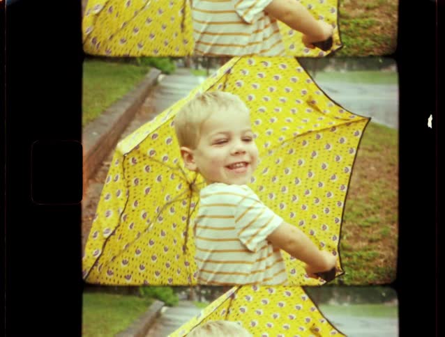 Vintage 8mm film shows a happy little boy smiling and playing with a yellow umbrella in the rain