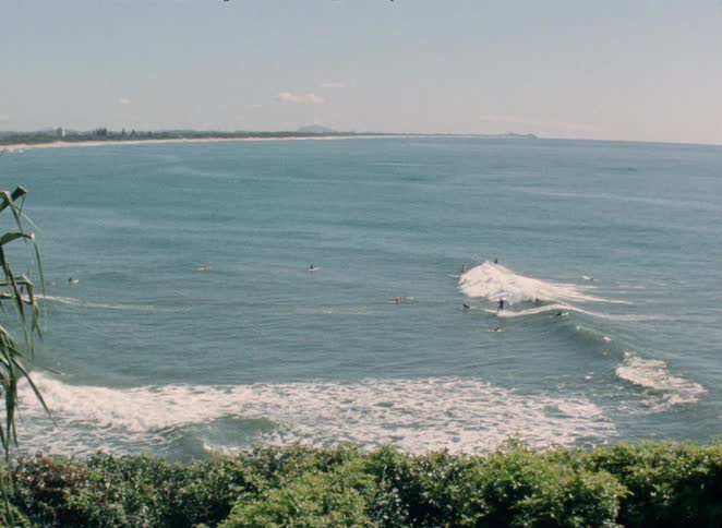 A beautiful wide shot from a high angle shows surfers enjoying the gentle ocean waves on a sunny day