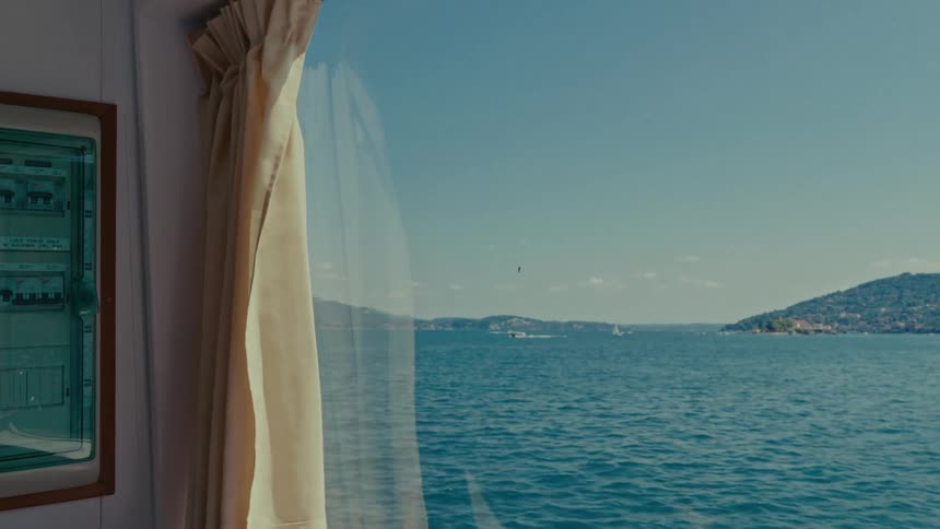 A scenic view of the sea and distant coastline from the window of a moving ferry on a sunny day