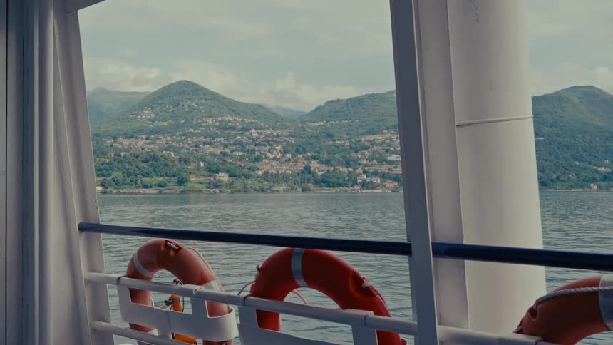 A scenic view from a ferry crossing a calm lake, looking out at a picturesque town nestled in the green mountains
