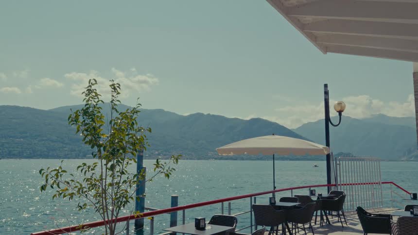 A peaceful view from an outdoor cafe patio overlooking a sparkling lake and distant mountains on a sunny day