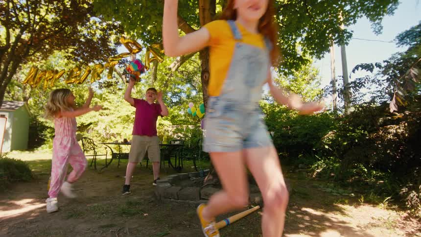 A young boy smashes a piñata at a backyard birthday party as his friends run to collect the candy