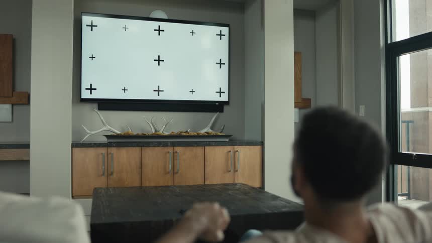 A man on a couch uses his smartphone before settling in to watch a large television with a screen ready for compositing