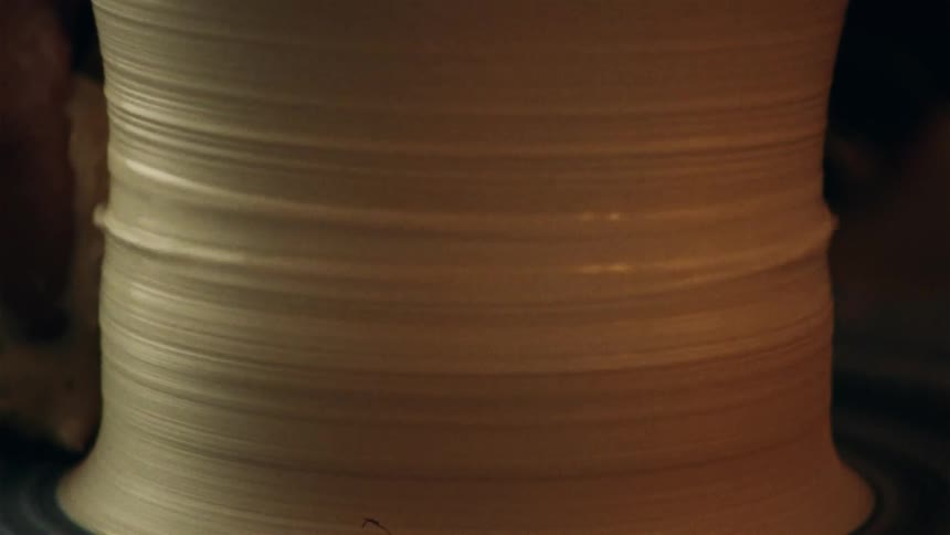 A close-up view of a potter's hands carefully shaping clay on a spinning wheel