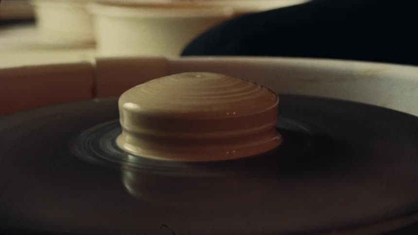 A close-up of a potter pouring liquid clay onto a spinning pottery wheel in a workshop