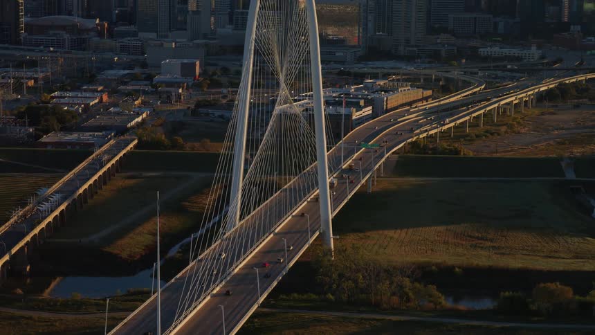 Golden hour aerial view slowly pushing in on the Margaret Hunt Hill Bridge with the Dallas city skyline in the background