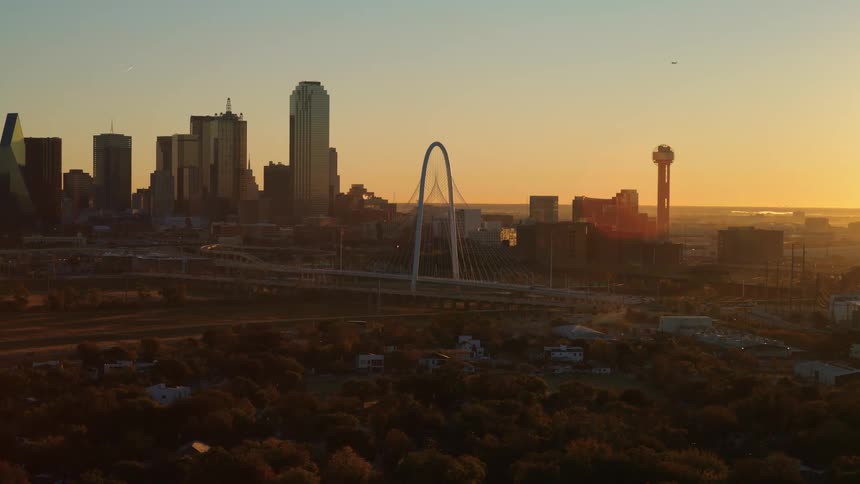 A slow aerial push-in shot reveals the iconic Dallas skyline, including Reunion Tower, bathed in the warm light of a beautiful sunset