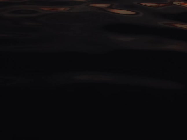 Dark, rippling water reflecting a warm sunset glow fades to black