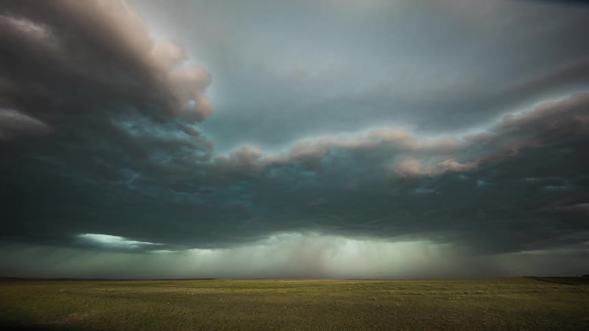 Storm clouds form and drop rain over a plain