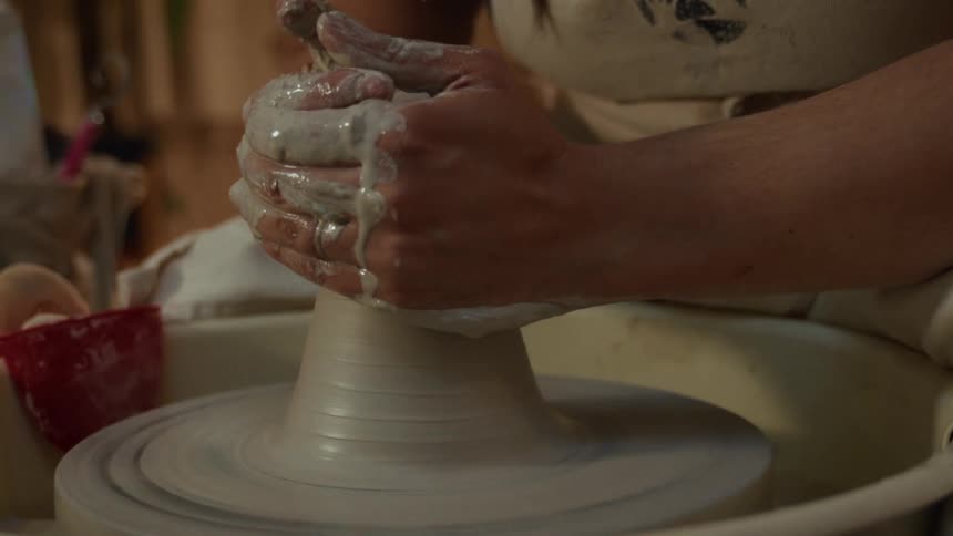 A potter's hands skillfully mold a lump of wet clay on a spinning wheel in a slow-motion close-up
