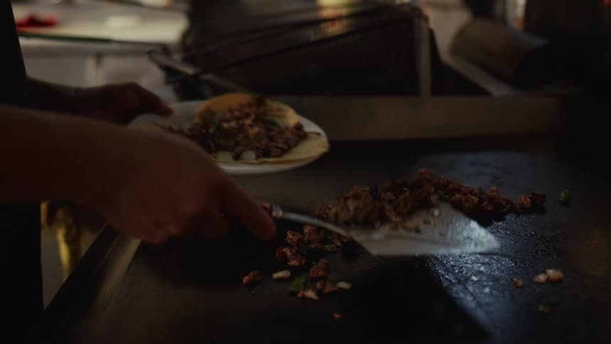 A street food vendor expertly serves sizzling meat onto fresh tortillas in slow motion