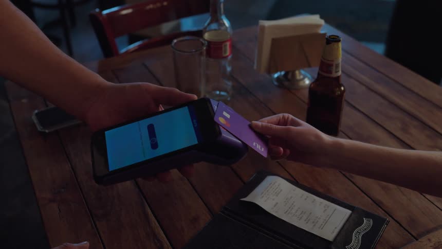 A customer makes a contactless payment with a credit card at a restaurant, tapping it on the waiter's POS terminal
