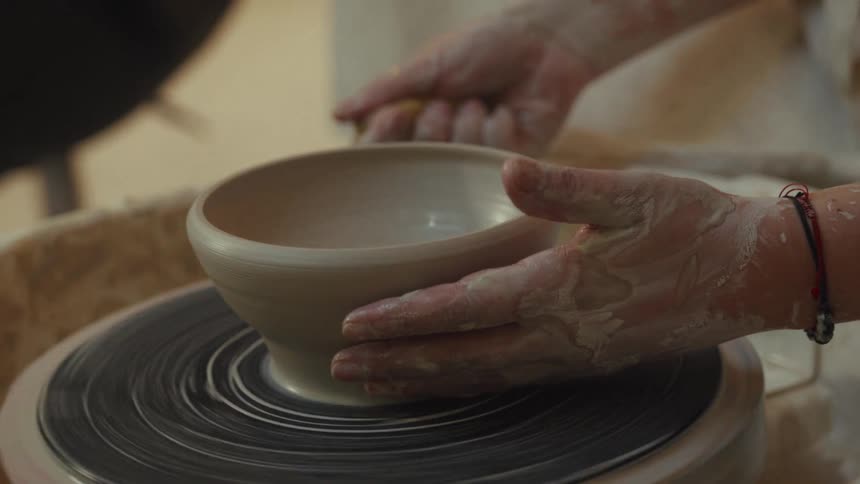 A potter's hands carefully sculpt a wet clay bowl as it spins on a pottery wheel