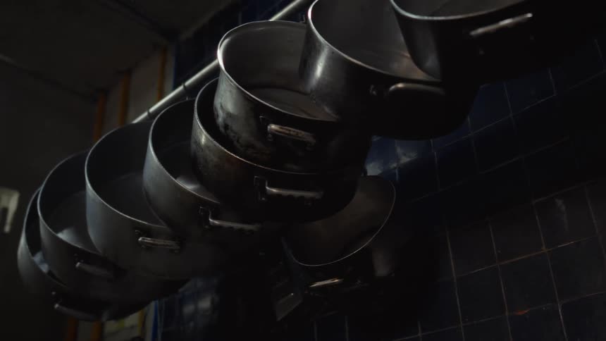 Well-worn metal stock pots hang from a rack in a dimly lit industrial kitchen