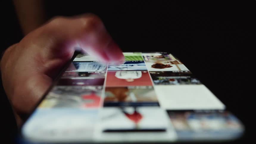 A close-up view of a finger scrolling endlessly through a social media feed on a smartphone in a dark room
