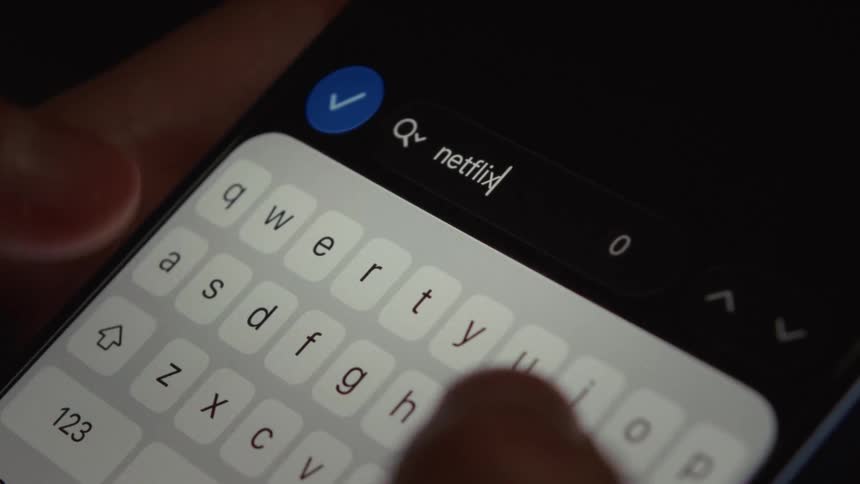 Close-up shot of fingers typing the word "netflix" into a search bar on a smartphone screen