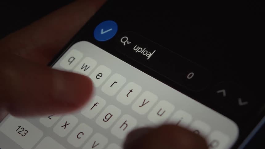 A close-up of a person typing 'upload' into a smartphone's search bar in dark mode