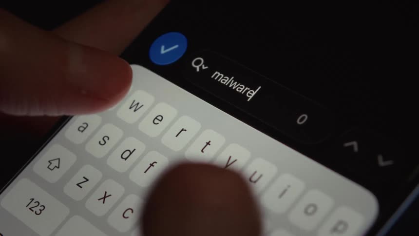 A close-up of a person typing the word 'malware' into a search bar on their smartphone