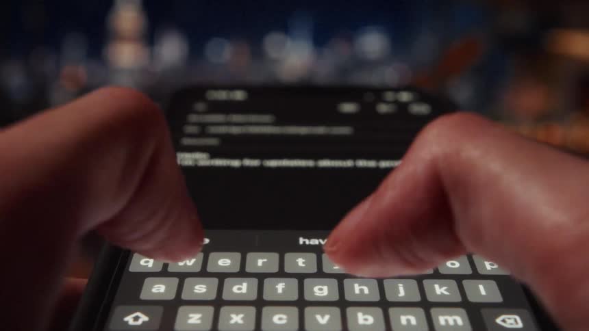 An extreme close-up shot of a person's hands typing an email on a smartphone at night