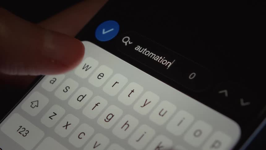 A person slowly types the word 'automation' into a search bar on a smartphone in slow motion
