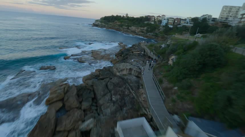A dynamic FPV drone flies over the famous Bondi Icebergs ocean pool and along the rocky coastal walk in Sydney at dusk