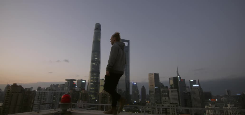 A man is walking along the rooftop at dawn