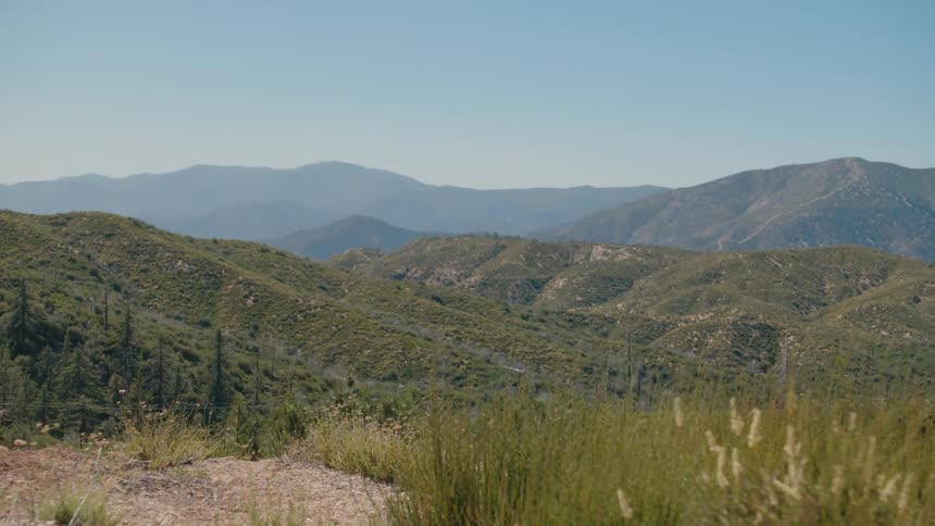 A beautiful scenic view from a mountain trail overlooks a vast range of green hills and mountains on a clear day