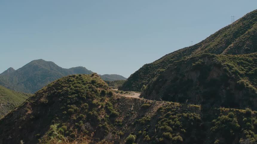 Flying through a sunny green canyon to reveal a motorcycle riding along a winding mountain road