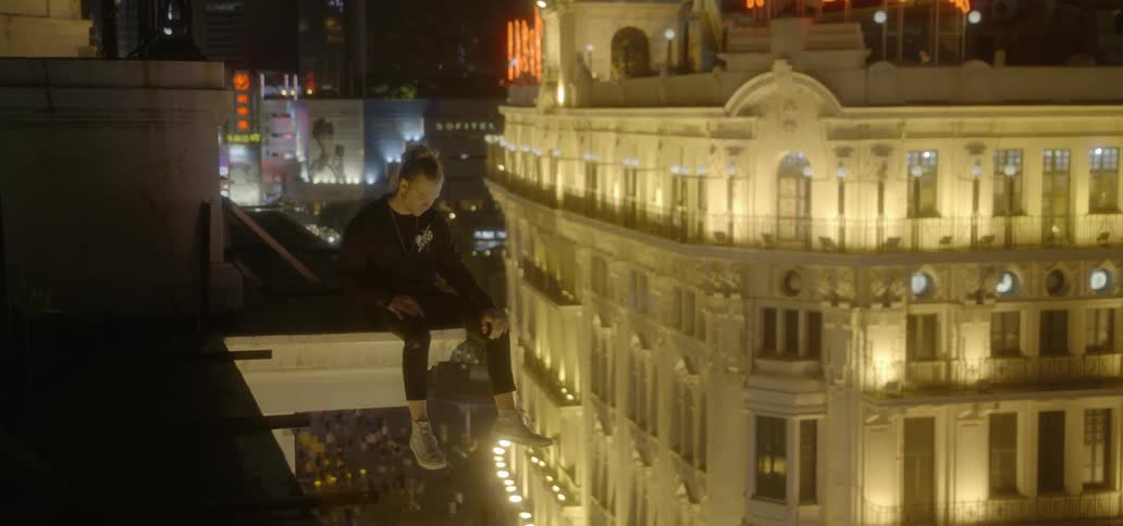 A man sits on the corner ledge of a building looking down at the city