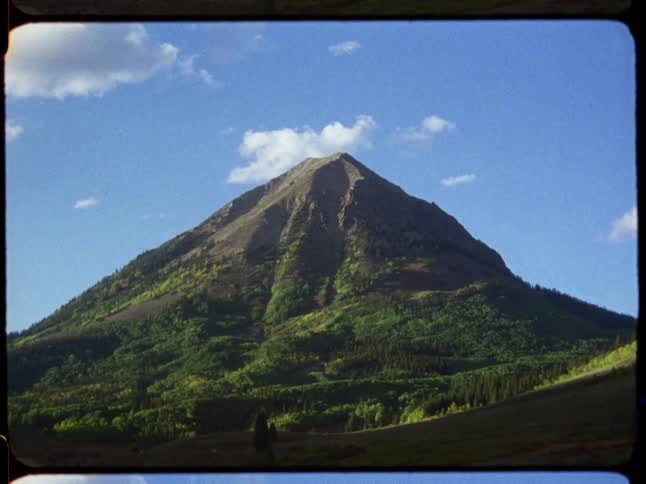 A vibrant red and orange vintage film burn effect fades to reveal a majestic green mountain under a partly cloudy sky