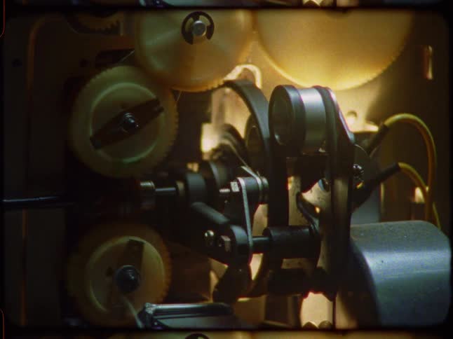 A close-up of the spinning gears and sprockets inside a vintage Super 8 film projector in operation