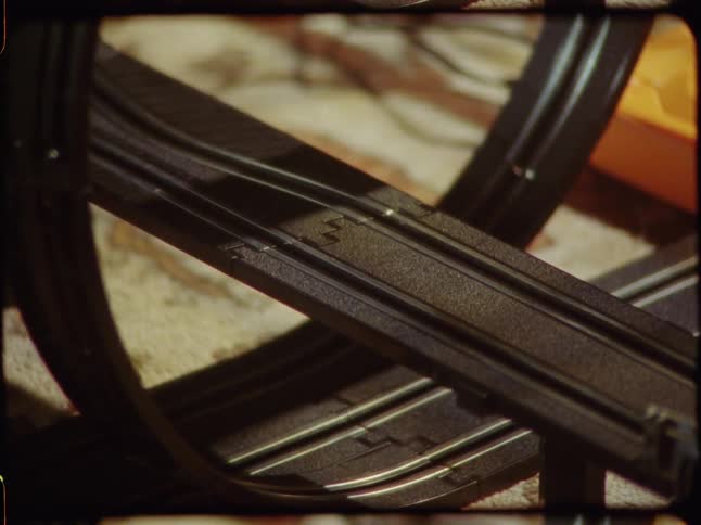A vintage 8mm film captures a close-up of red and yellow slot cars racing at high speed on a classic toy track