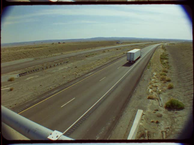 Vintage high-angle shot captures a semi-truck driving along an empty highway through a vast desert landscape