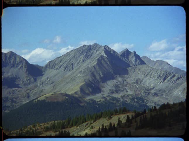 A vintage film shot captures the majestic Rocky Mountains standing tall against a bright blue sky