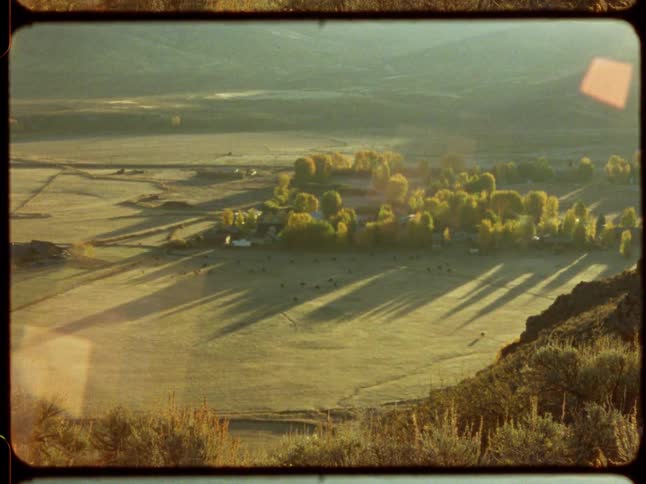 A static archival film shot shows a rural valley basking in the golden morning sun, with long shadows stretching across the fields