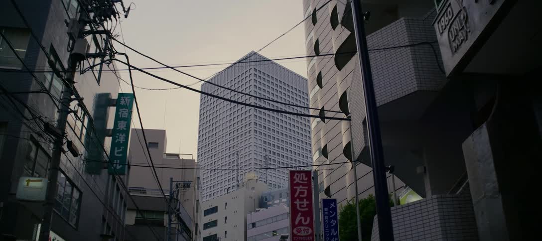 A slow zoom towards a towering skyscraper in a dense urban neighborhood in Tokyo, Japan, on an overcast day