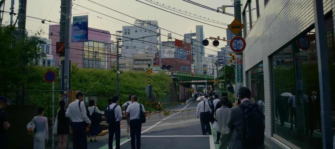Commuters and pedestrians wait patiently for a passing train at a railroad crossing in a bustling Tokyo neighborhood before continuing on their way