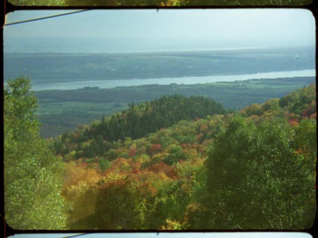 Vintage film captures a scenic view of a river valley with colorful autumn foliage covering the rolling hills