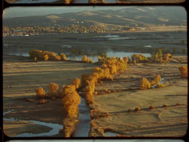 Vintage film footage shows an aerial view zooming out over a misty river valley filled with vibrant yellow autumn trees at sunrise