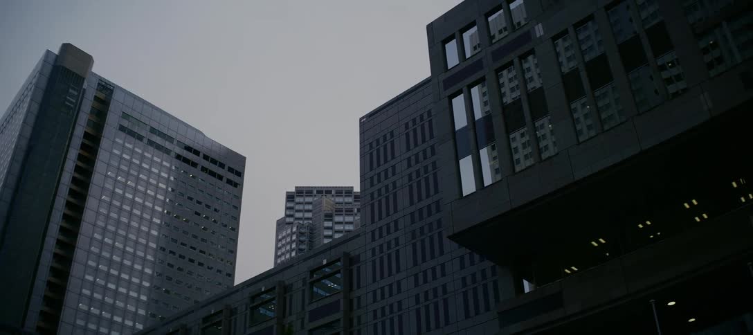 Dolly shot past a red traffic light revealing the towering, modern architecture of a city on a gloomy, overcast day