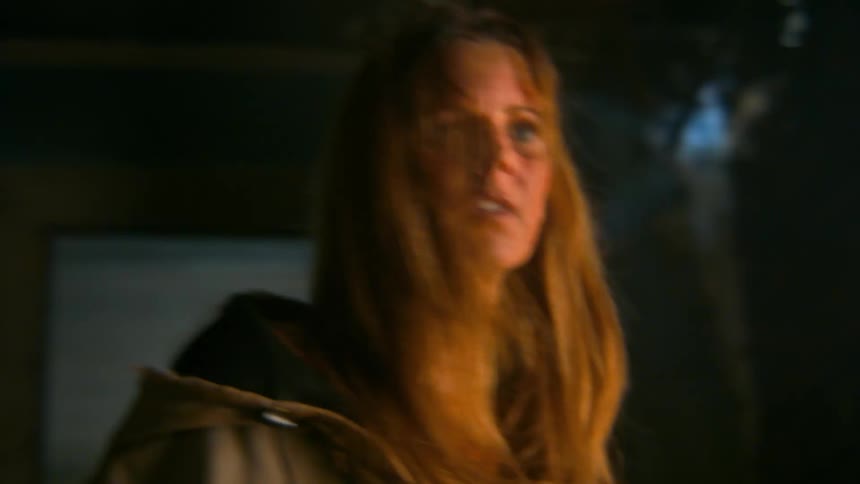 A terrified and disheveled woman breathes heavily in a dark, scary room, looking around frantically in a moment of panic