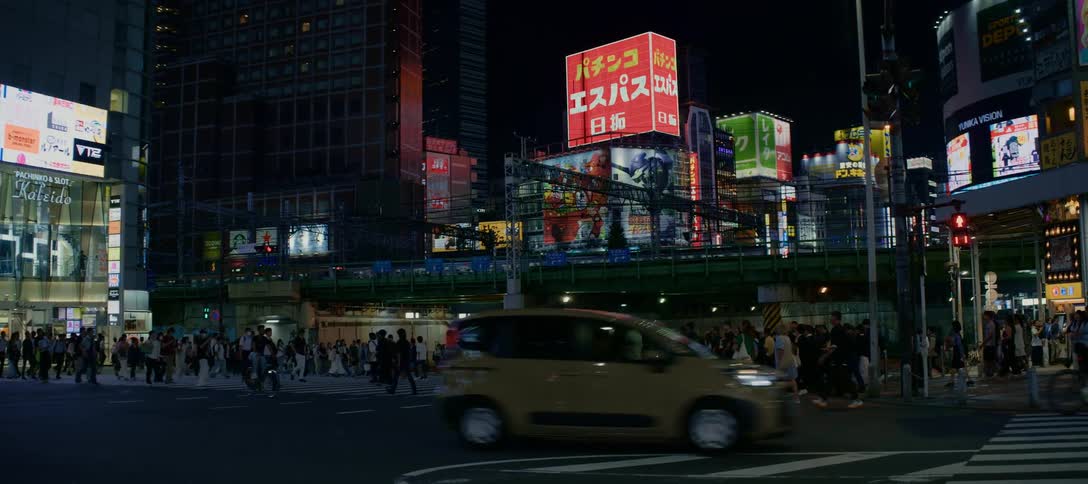 A slow tilt down reveals a busy intersection in Tokyo at night, with crowds of people crossing the street under vibrant neon signs and an elevated train passing by