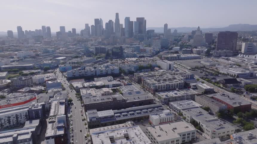 Aerial footage slowly flies over a train yard and urban landscape towards the downtown Los Angeles skyline on a sunny day