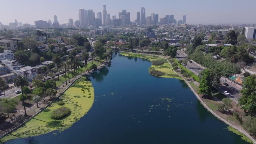 Slowly flying over the scenic Echo Park Lake, this aerial shot reveals the iconic Downtown Los Angeles skyline on a beautiful sunny day
