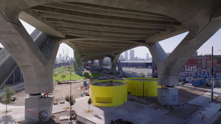 Aerial dolly shot moving forward under the modern concrete structure of the 6th Street Viaduct in Los Angeles during park construction