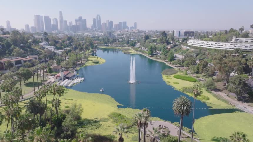 A sweeping aerial view reveals the iconic Echo Park Lake and its fountain, with the downtown Los Angeles skyline sitting on the horizon