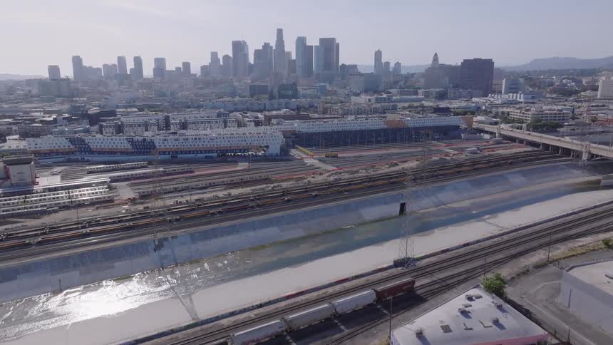 Aerial flight over the Los Angeles River and train yards towards the downtown Los Angeles city skyline